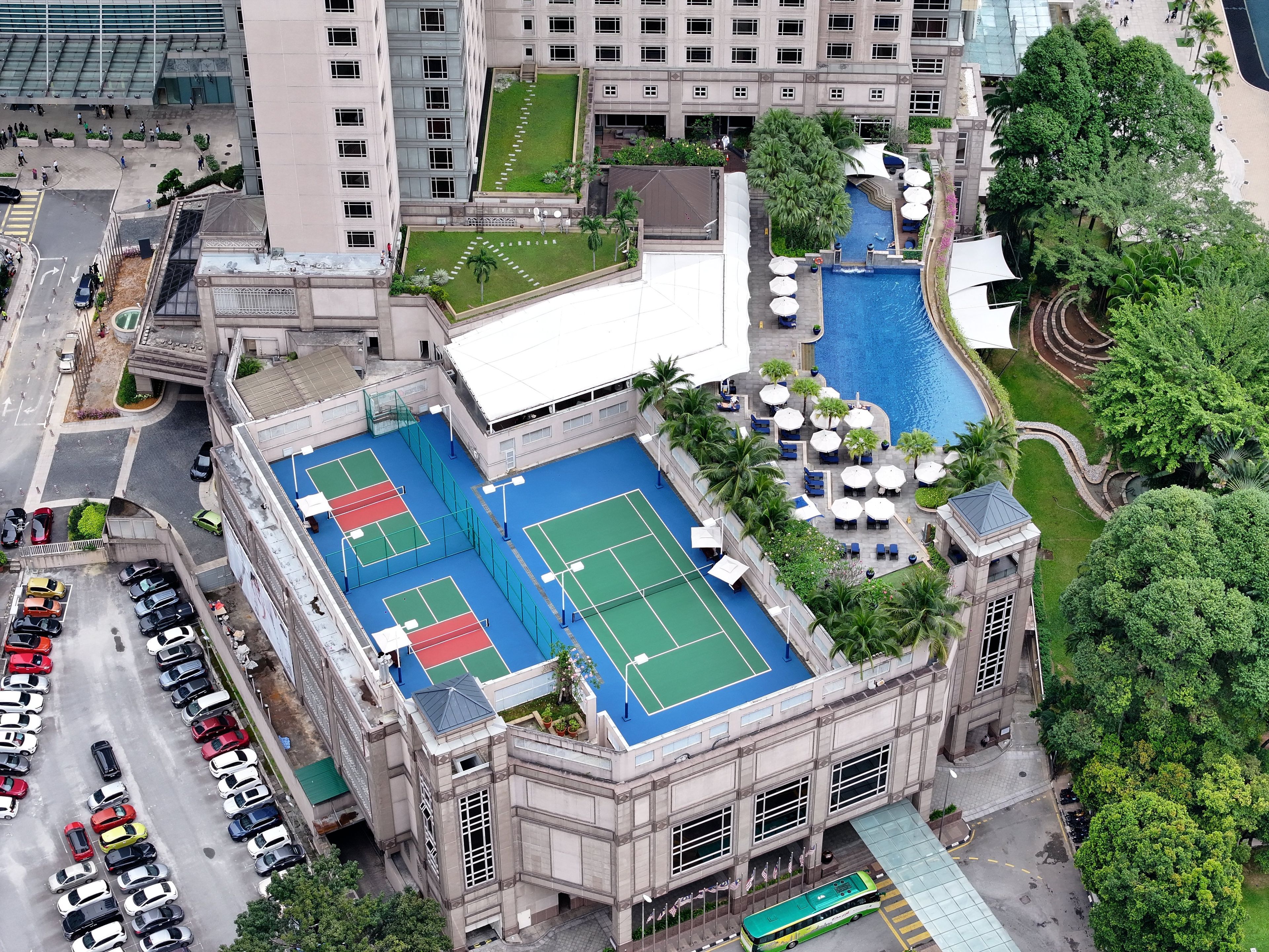 Un edificio de varios pisos con cancha de tenis en la azotea, piscina y área de estacionamiento.