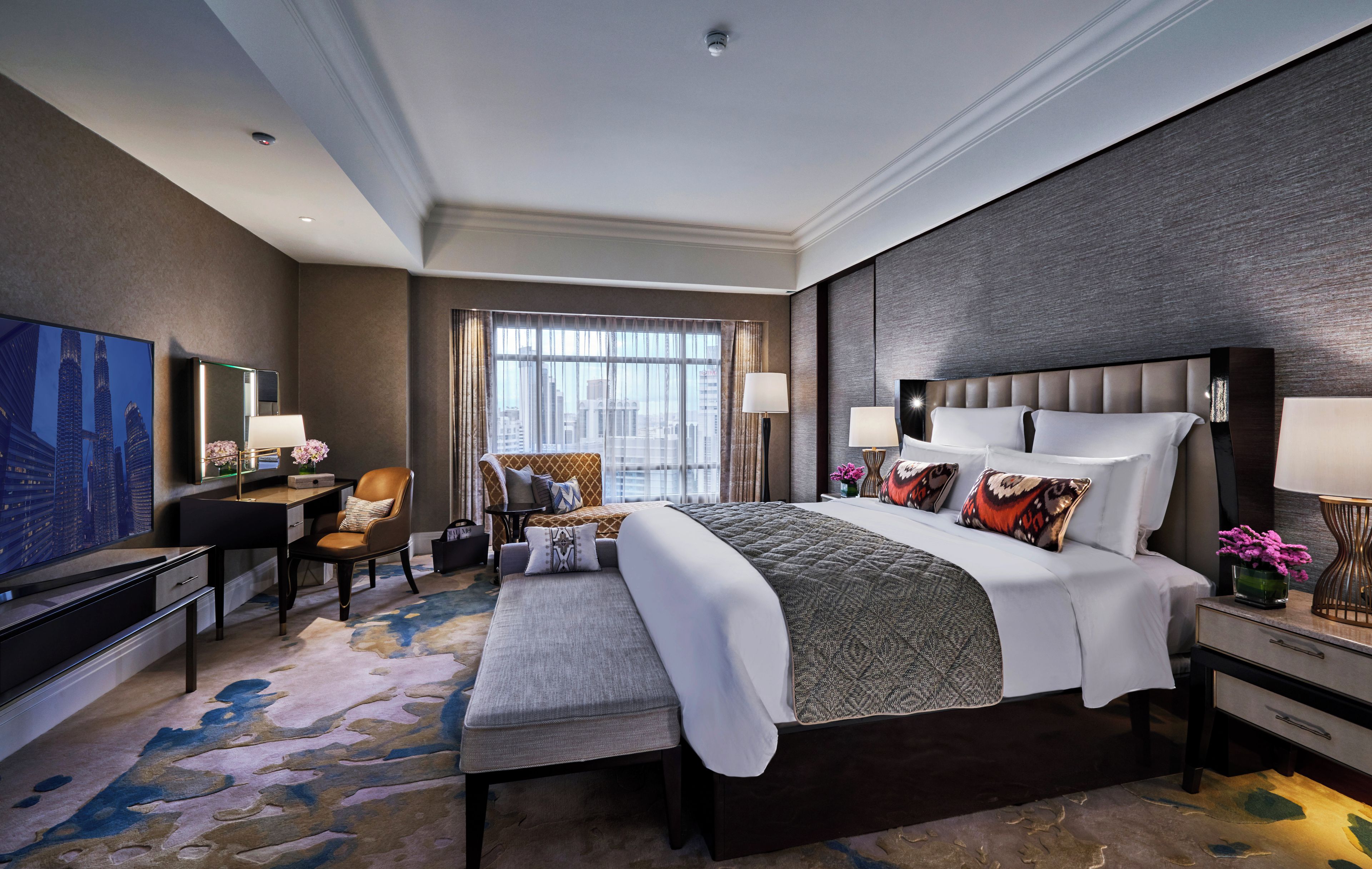 A modern hotel room with a large bed, a desk, a chair, and a television.