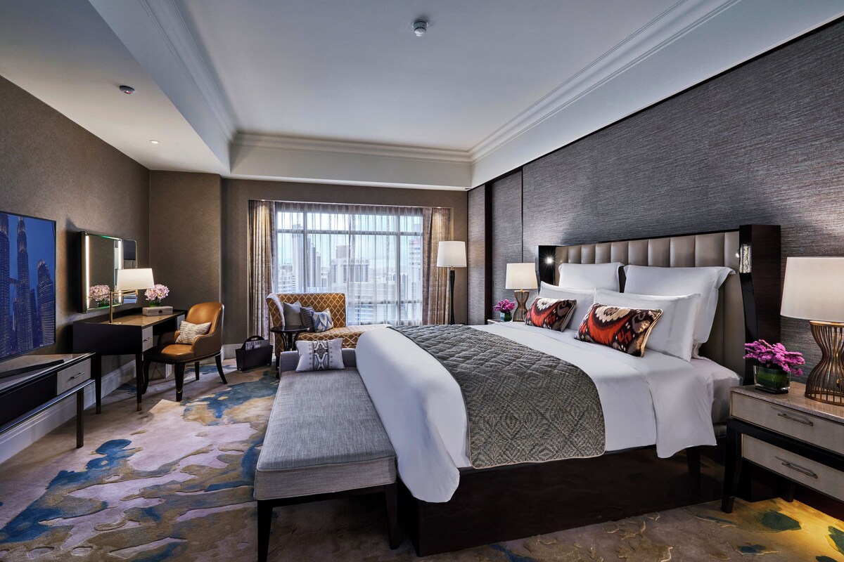 A modern hotel room with a large bed, a desk, a chair, and a television.