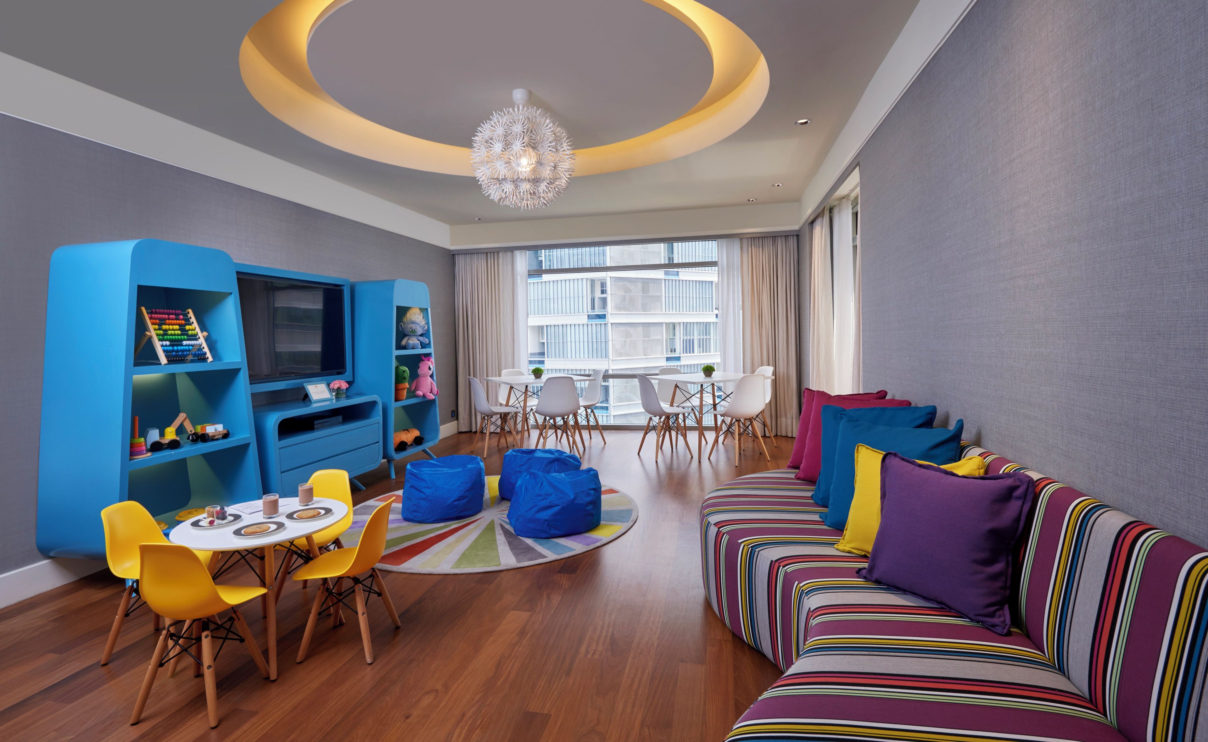 A modern living room with a blue entertainment unit, a round coffee table, colorful sofas, and a chandelier.
