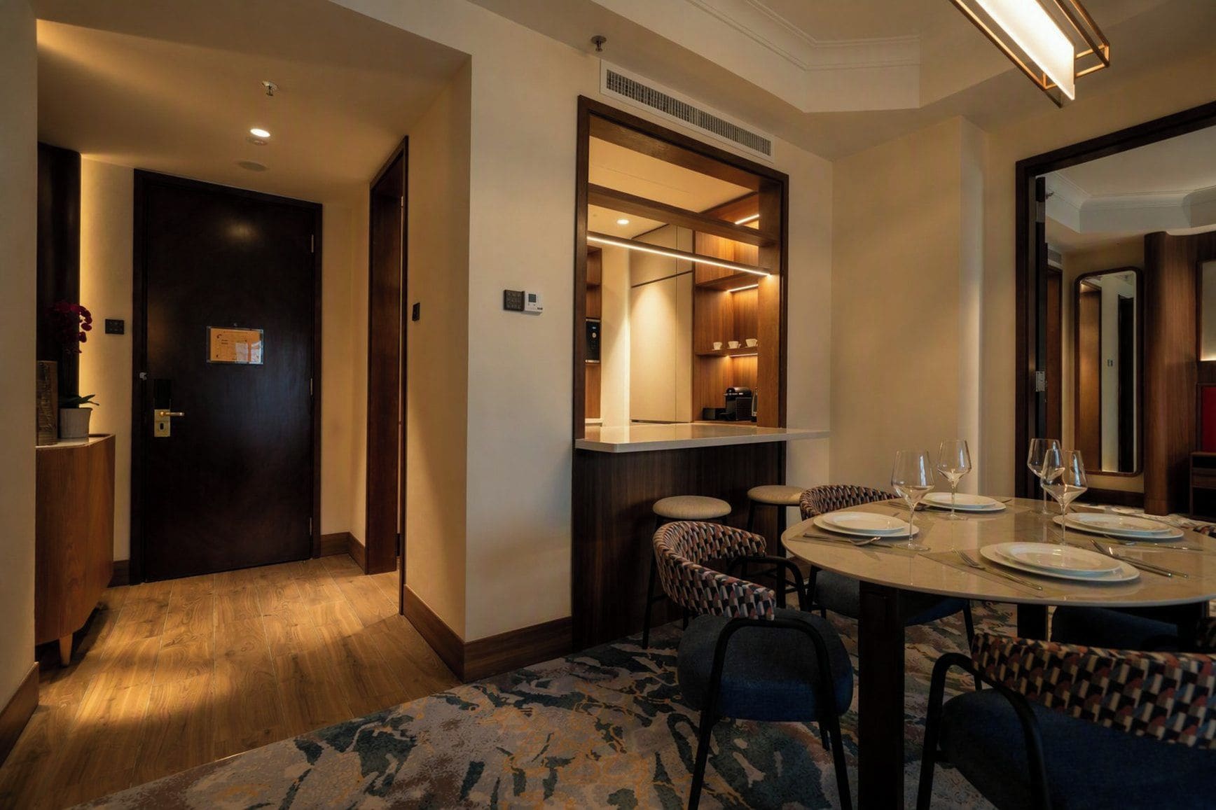 A hotel room with a dining area, a wooden door, a small plant, and a mirror.