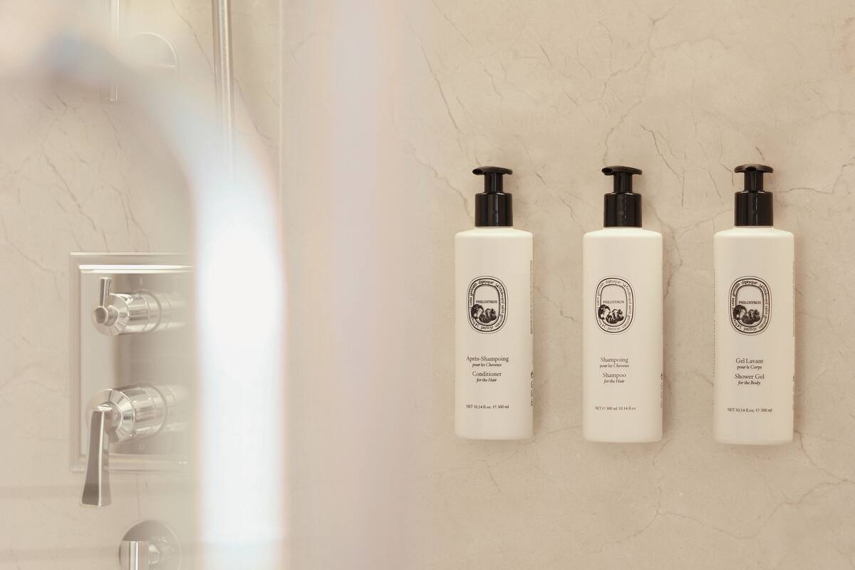 A bathroom with a shower, three bottles of shampoo, and a faucet.
