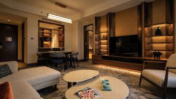 Een hotelkamer met een bank, twee ronde salontafels, een televisie en een zithoek met stoelen en een tafel.