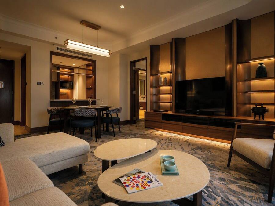 Een hotelkamer met een bank, twee ronde salontafels, een televisie en een zithoek met stoelen en een tafel.