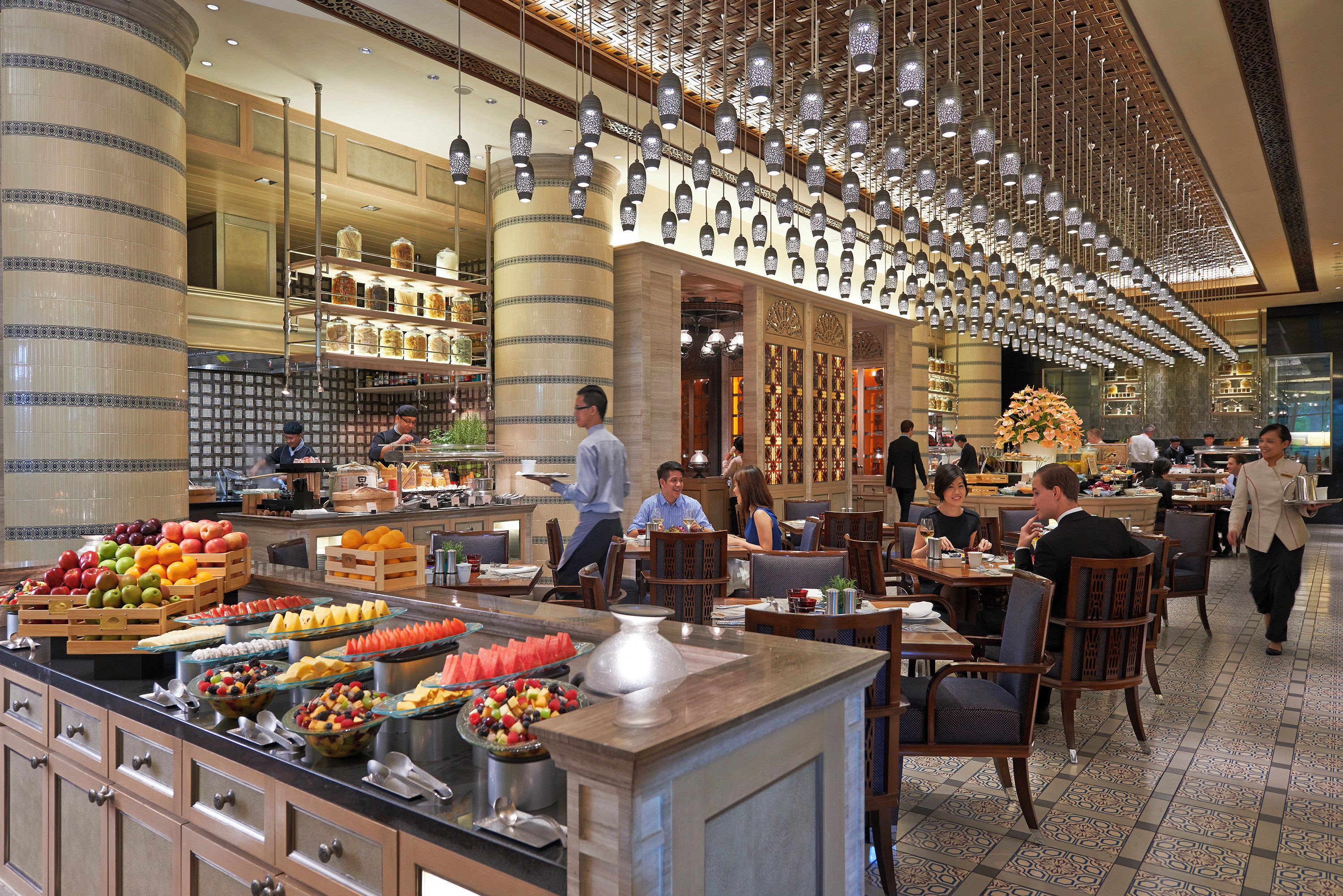 A hotel lobby with a central food display, seating areas, and a decorative ceiling.