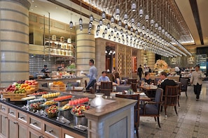 Un hall d’hôtel doté d’un présentoir central où sont exposés des plats, de coins salon et d’un plafond décoratif.