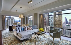 Amplia sala de estar con un sofá grande, una mesa de centro y un sillón, con vistas a la ciudad a través de amplias ventanas.