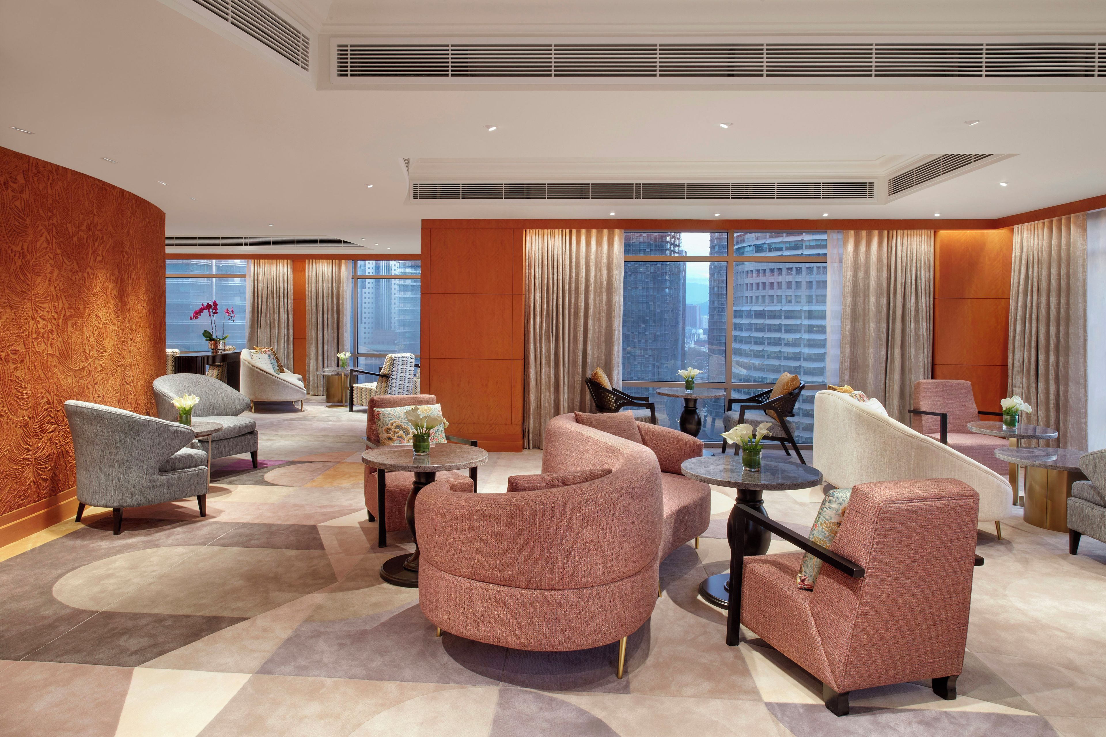 A hotel lobby with a modern design, featuring a mix of seating arrangements, a large window offering a city view, and a decorative wall.