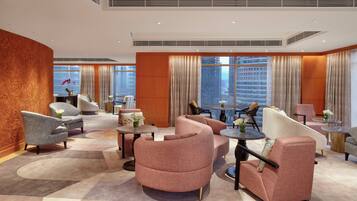 A hotel lobby with a modern design, featuring a mix of seating arrangements, a large window offering a city view, and a decorative wall.