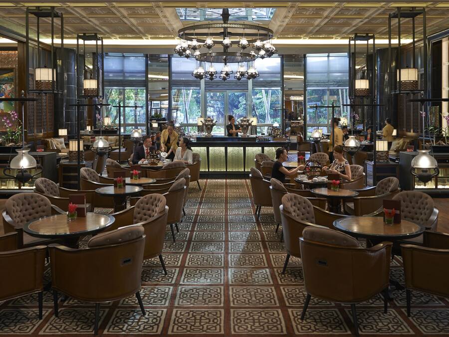 A spacious restaurant with round tables and cushioned chairs, a central bar area, and large windows offering a view of the outdoors.