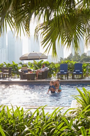 Un espace aménagé au bord de la piscine, avec des chaises longues, un jacuzzi et une vue sur les grands immeubles qui se dressent à l’arrière-plan.