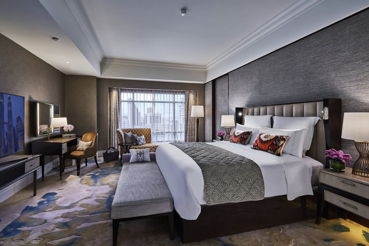 Ein geräumiges Hotelzimmer mit einem großen Bett, einem Schreibtisch, einem Stuhl, einem Fernseher und einem großen Fenster mit Vorhängen.