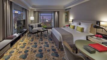 A hotel room with a large bed, a desk, a chair, a TV, and a view of the cityscape.
