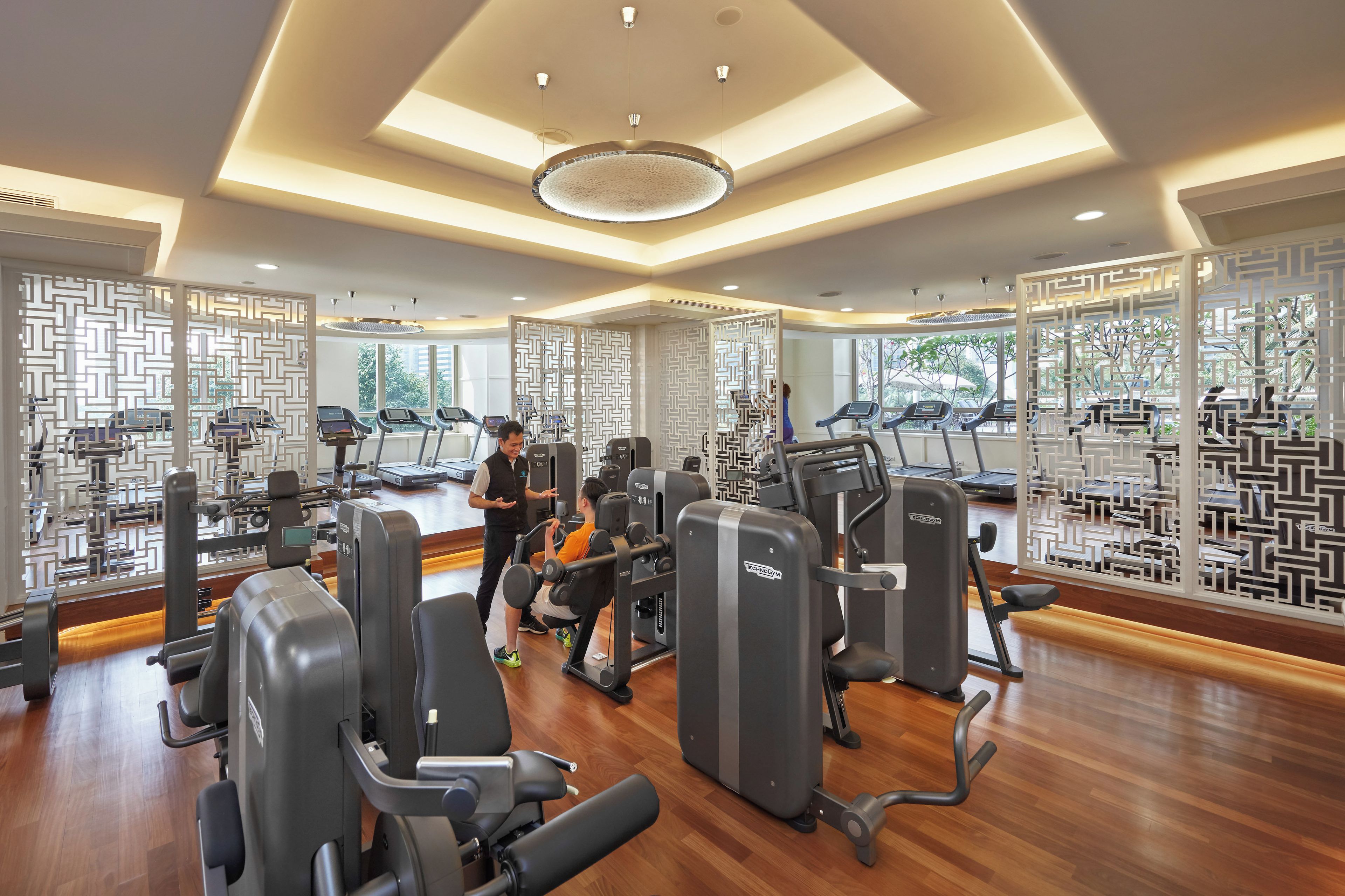 Ein modernes Fitnessstudio mit verschiedenen Trainingsgeräten, großen Fenstern und Holzboden.