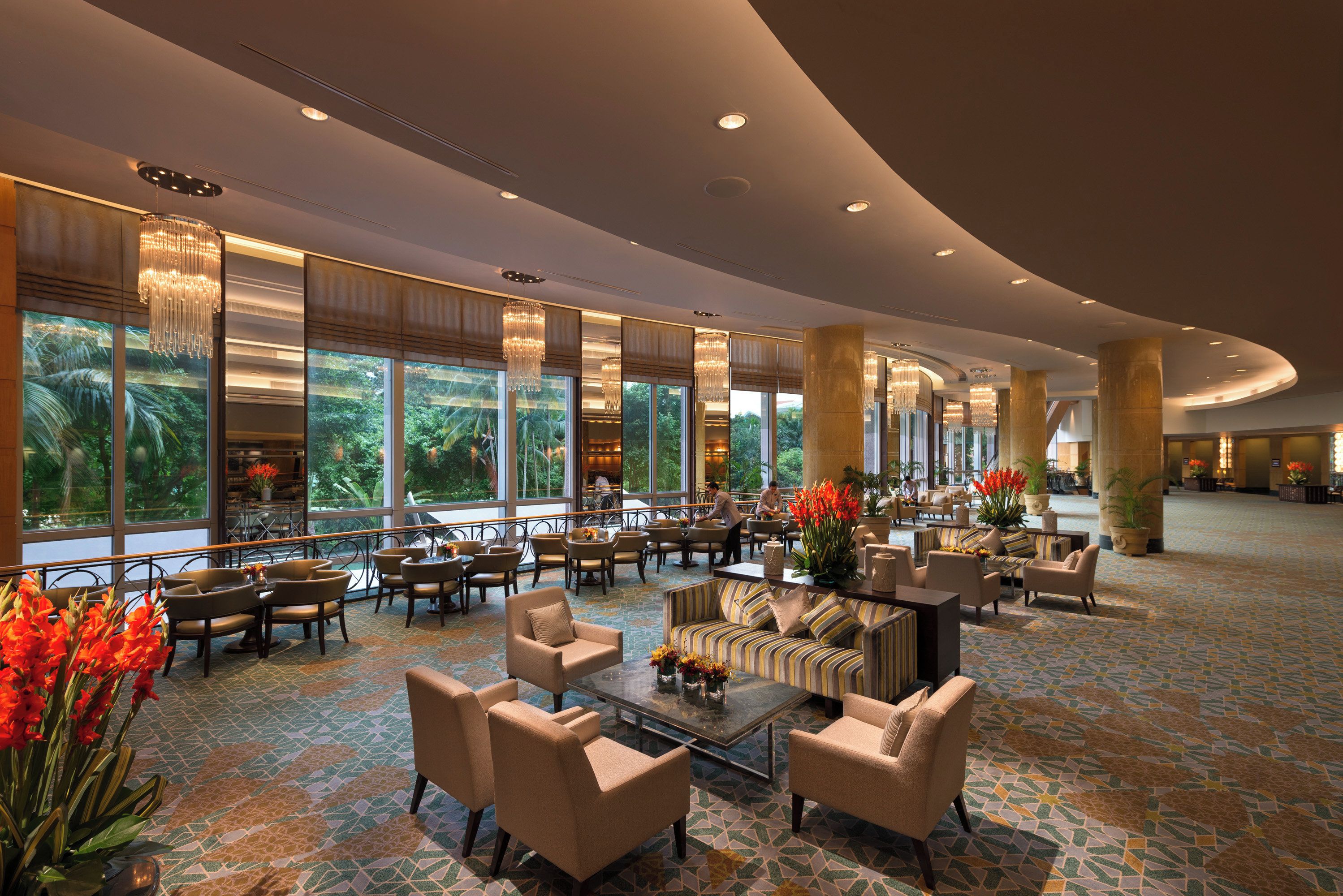 A spacious lobby with a high ceiling, large windows, and a central seating area with sofas and chairs.