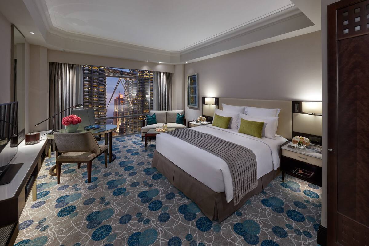 Ein Hotelzimmer mit einem großen Bett, einem Schreibtisch, einem Sessel, einem Fernseher und Blick auf die Stadt.