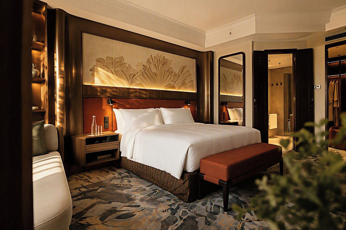 A hotel room with a large bed, a nightstand, a bedside table, a bench, a mirror, and a wardrobe.