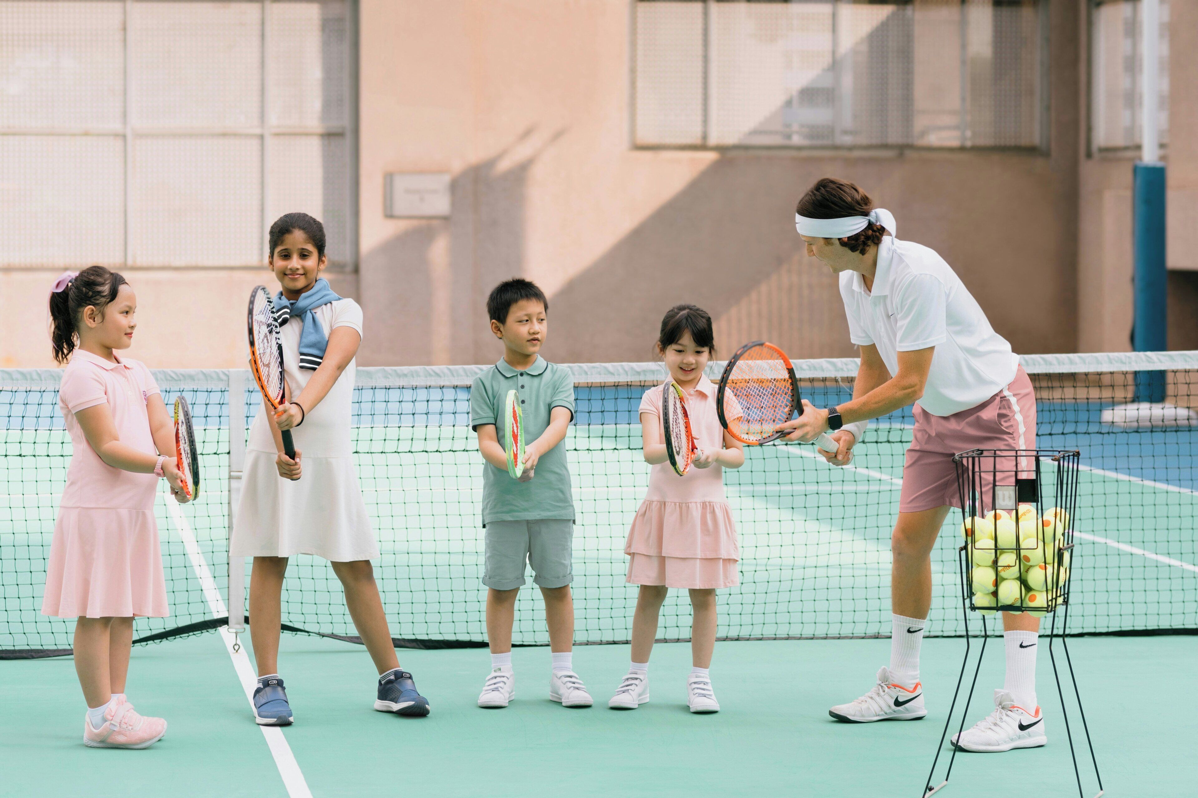 Un court de tennis avec un filet, un porte-balles rempli de balles de tennis et des joueurs tenant des raquettes.
