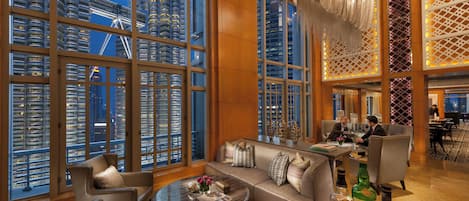 Un amplio hall de hotel con un diseño moderno, que cuenta con un amplio espacio para sentarse, un bar y vistas de la ciudad a través de amplias ventanas.