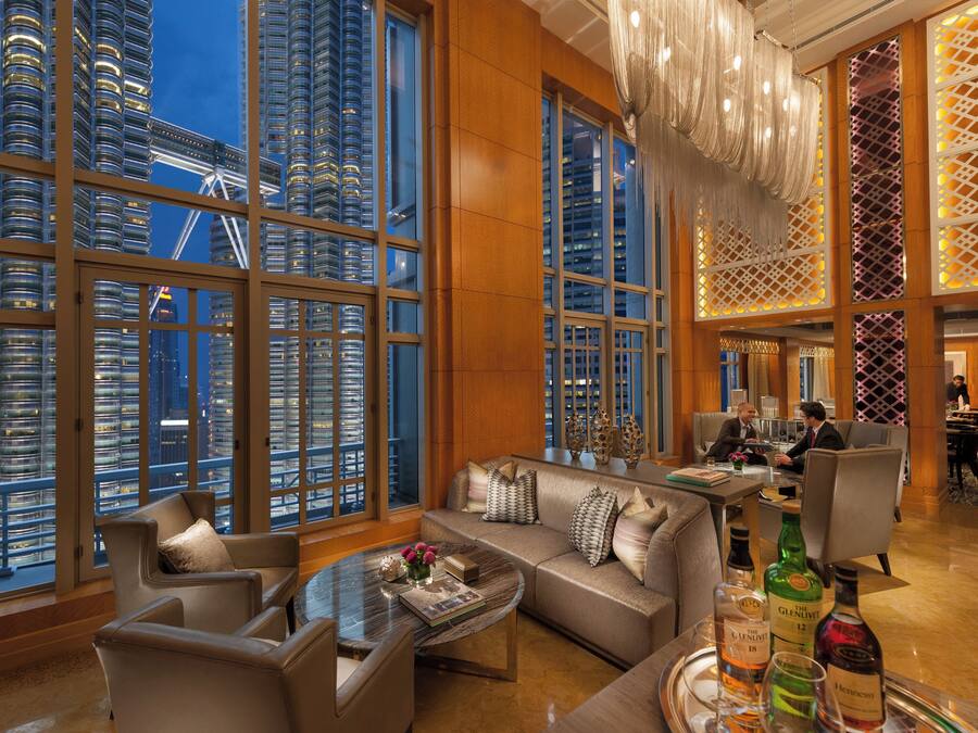 A spacious hotel lobby with a modern design, featuring a large seating area, a bar, and a view of the cityscape through expansive windows.