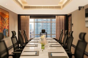 A conference room with a long table, chairs, a projector, and a view of high-rise buildings.