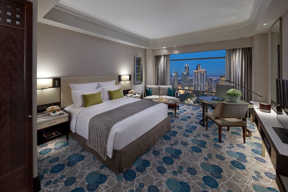 Ein Hotelzimmer mit einem großen Bett, einem Schreibtisch, einem Stuhl und Blick auf eine Stadtlandschaft.