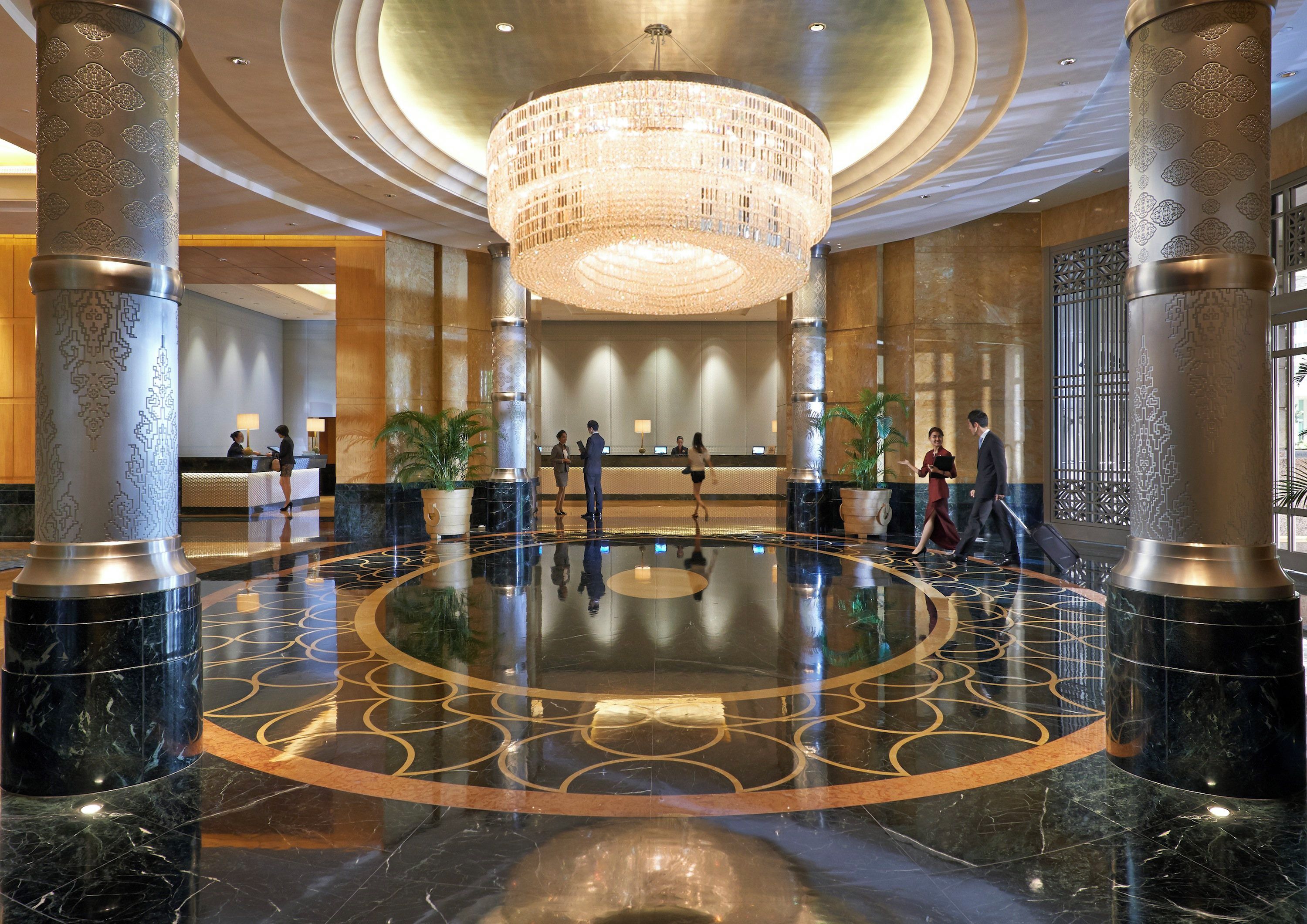 A lobby with a central chandelier, marble flooring with geometric patterns, and a reception desk.