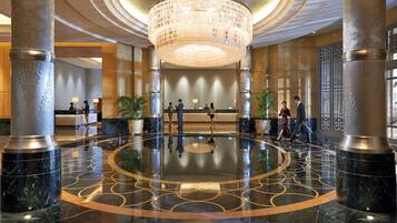 A lobby with a central chandelier, marble flooring with geometric patterns, and a reception desk.