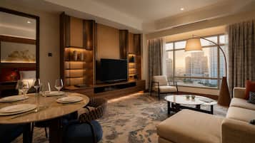 A hotel room with a flat-screen TV, a dining table set with plates and glasses, a sofa, a chair, and a large window with a city view.