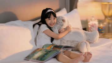 A person sitting on a bed with a book and a stuffed animal.