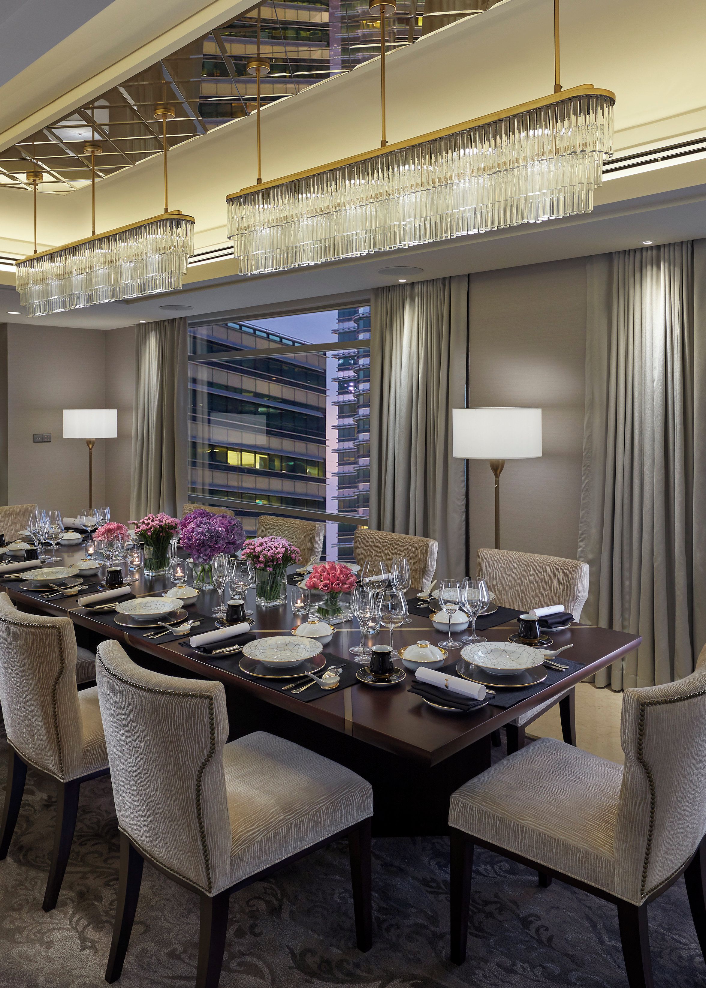 A dining room with a long table set for a meal, featuring chairs, plates, cutlery, and a chandelier.