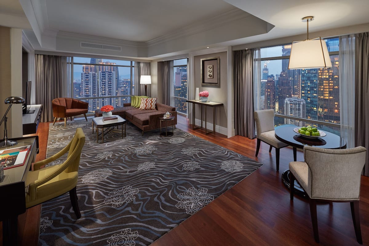 Ein modernes Hotelzimmer mit Blick auf die Stadt, einer Couch, einem Esstisch und einer Arbeitsnische mit Schreibtisch und Stuhl.