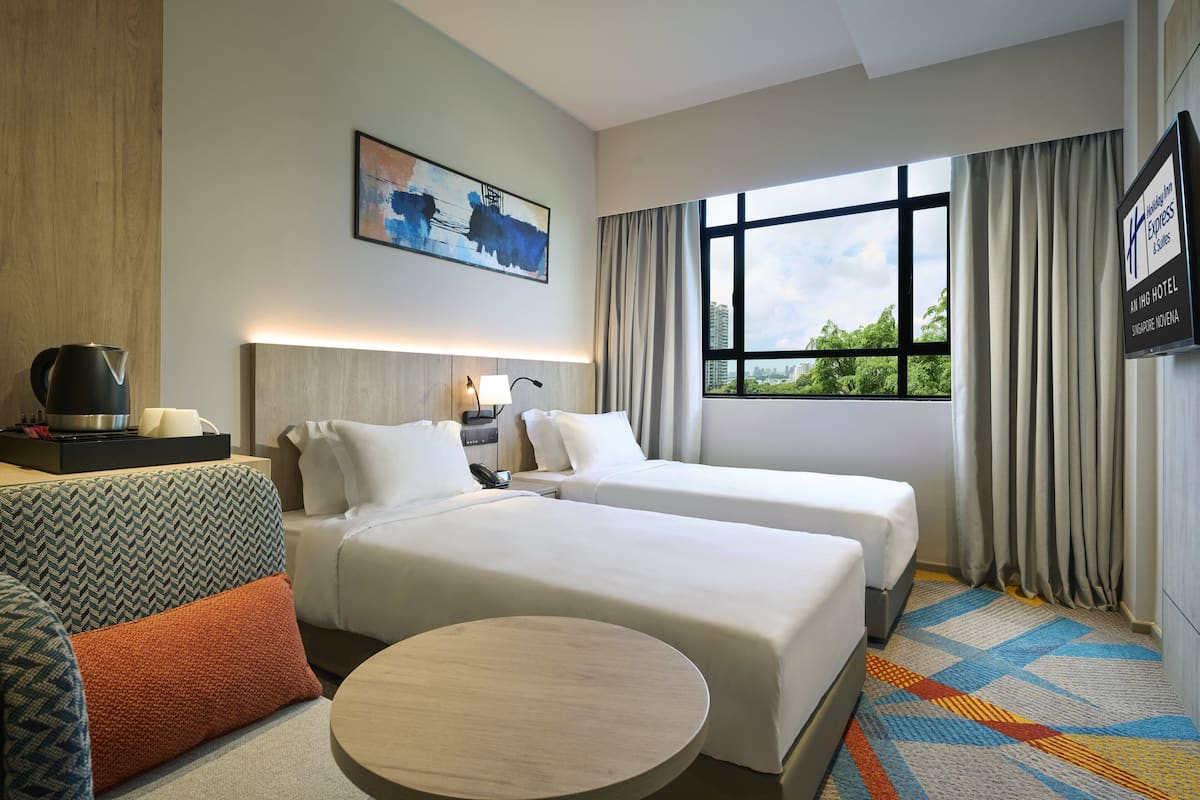 Een hotelkamer met twee bedden, een bank, een ronde tafel, een schilderij aan de muur en uitzicht op groen door het raam.