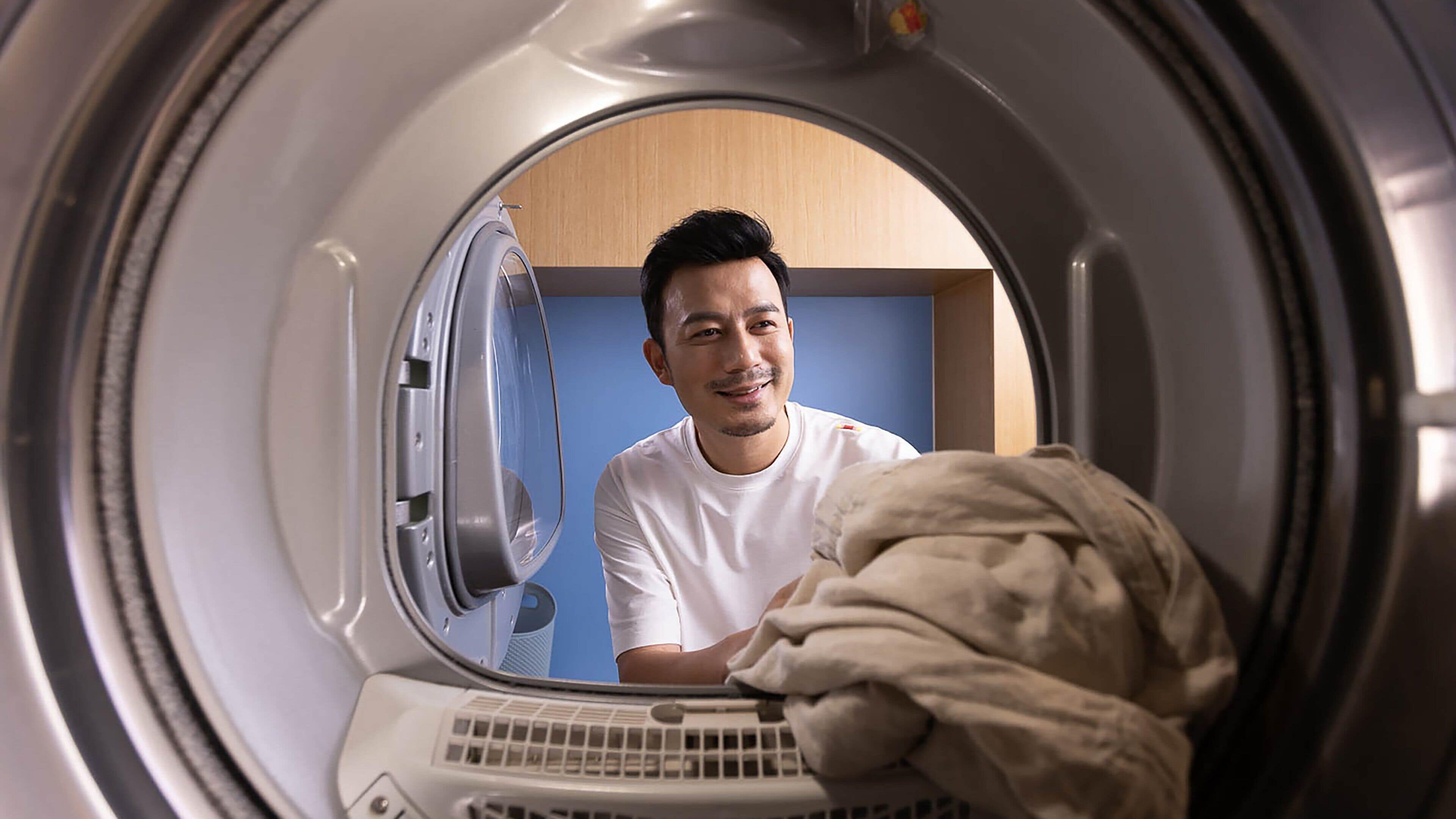 A person inside a front-loading washing machine with a blue wall in the background.