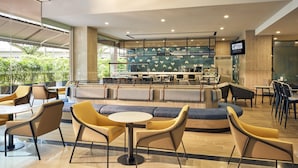 Een moderne hotel lobby met zithoeken, een bar en uitzicht op groen.