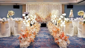 Een feestzaal met gedekte tafels voor een formeel evenement, versierd met bloemstukken en een blauw tapijt.