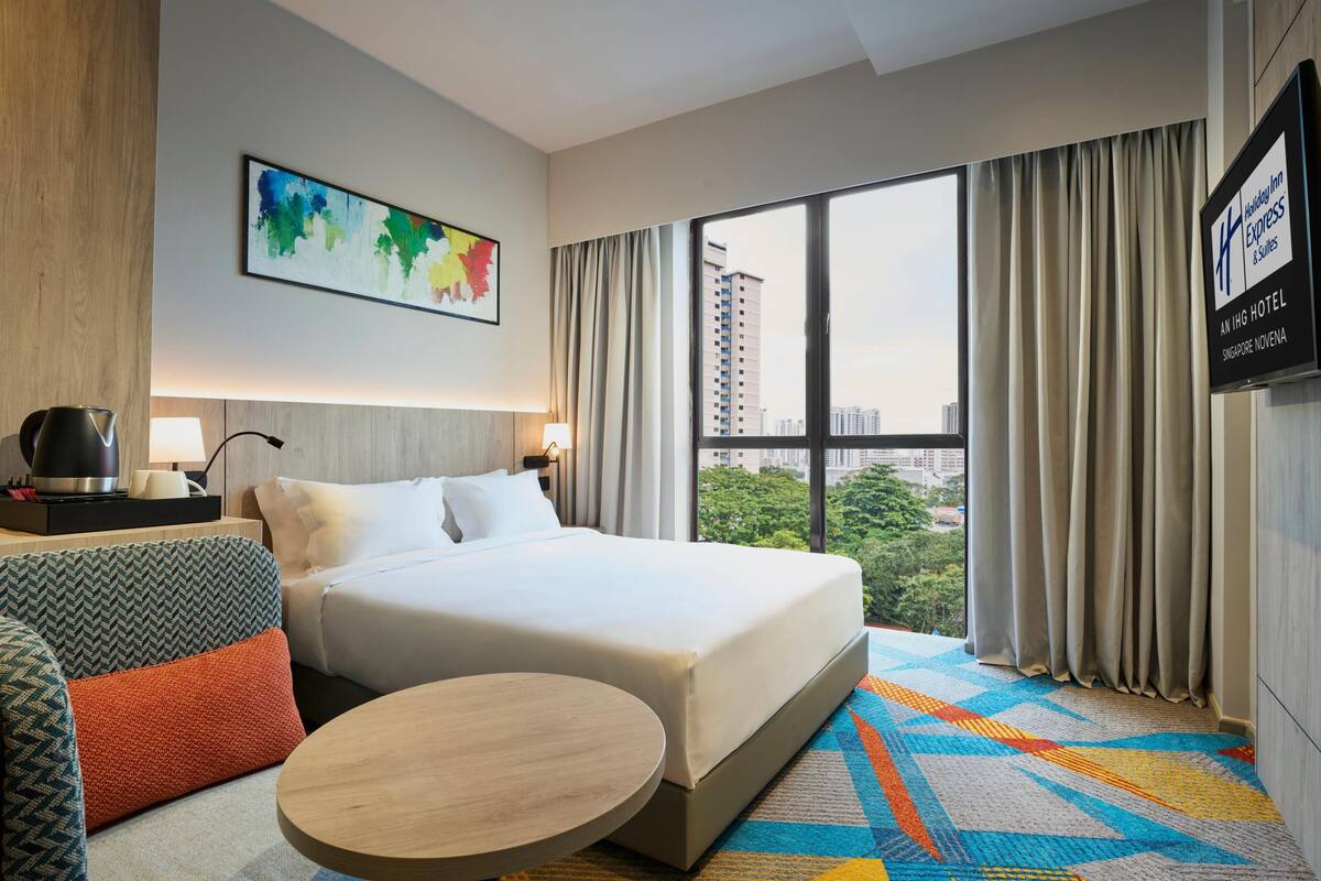 Une chambre d’hôtel avec un lit, un canapé, une table ronde, un tableau et une vue sur la ville.