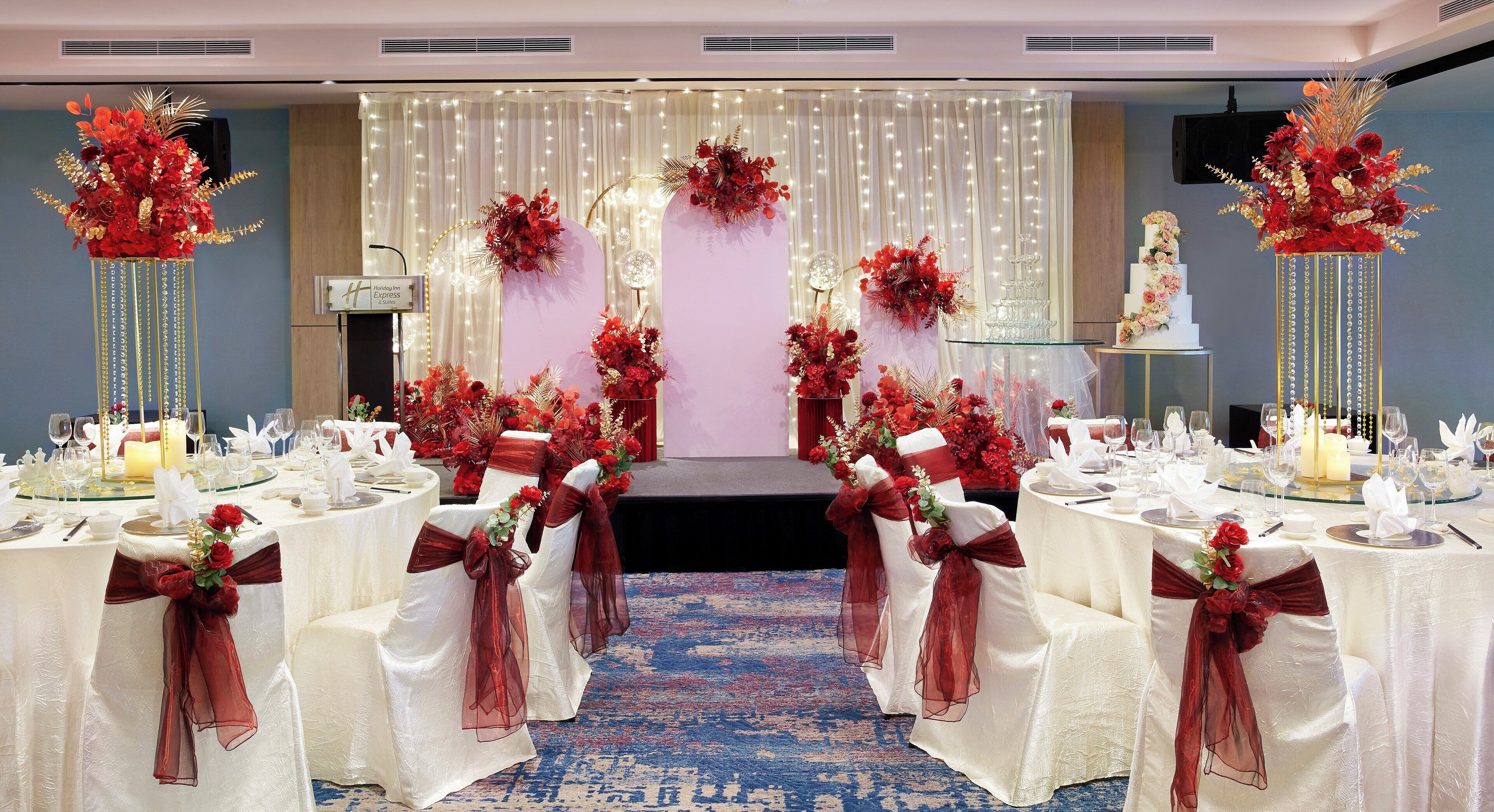 A banquet hall with white tables, red sashes, and floral centerpieces.