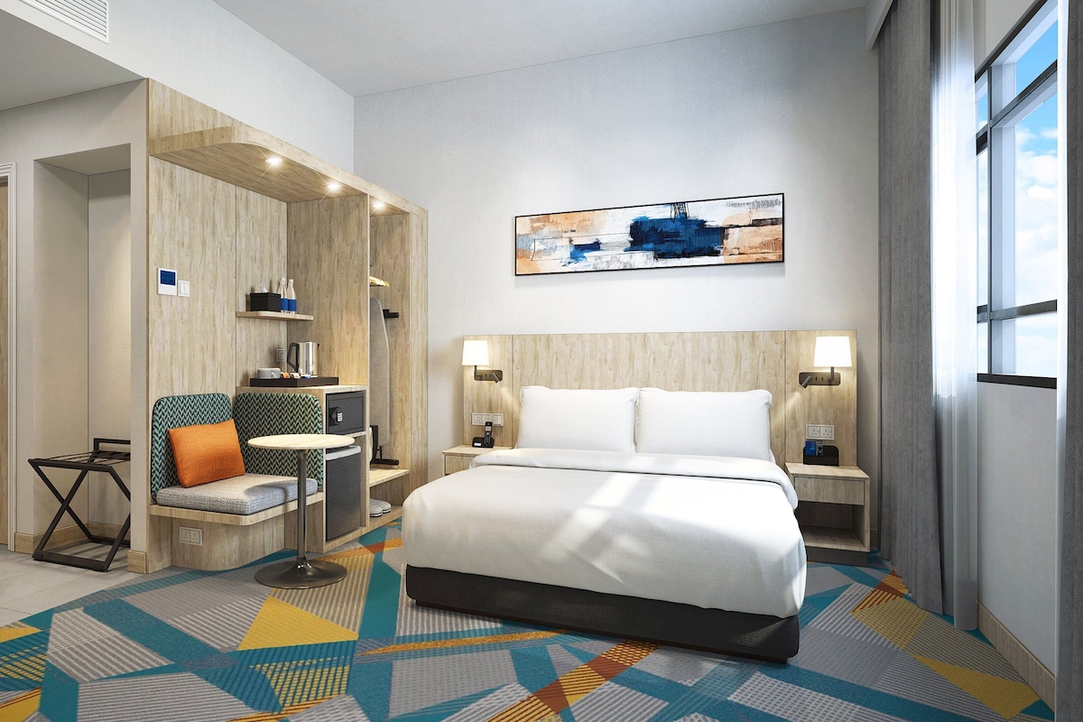 Ein modernes Hotelzimmer mit einem großen Bett, einer Sitzecke mit Tisch und einem Bild an der Wand.