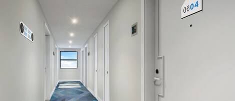 Un pasillo moderno de hotel con alfombra de estampado geométrico, paredes blancas y puertas numeradas 0605, 0601, 0609, 0604.