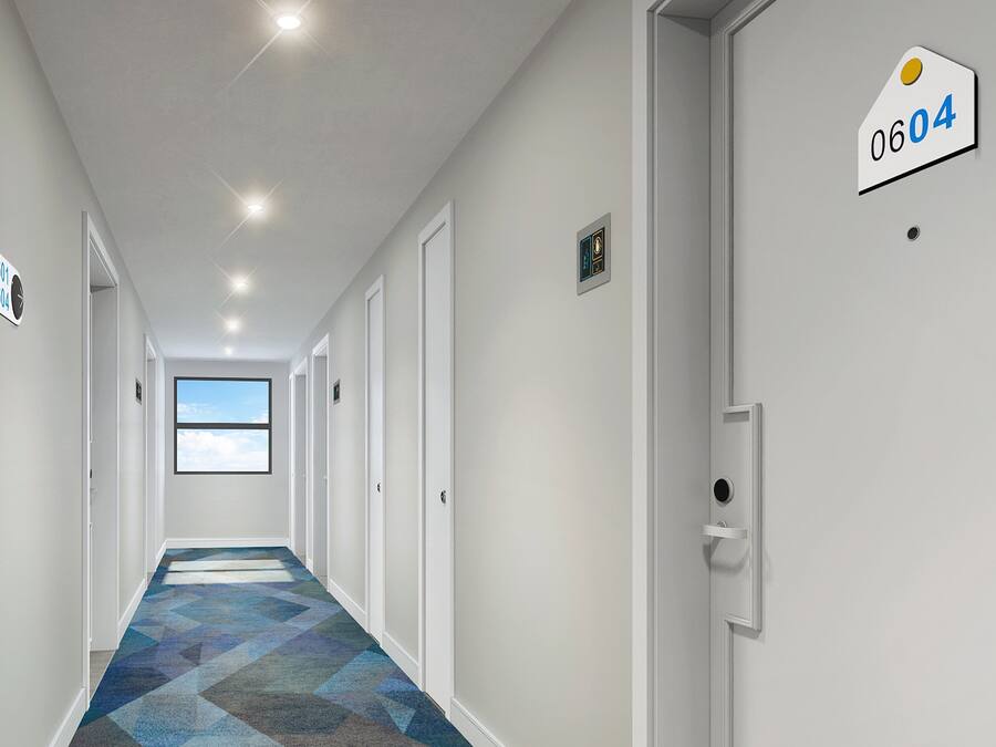 A modern hotel hallway with a geometric patterned carpet, white walls, and doors numbered 0605, 0601, 0609, 0604.