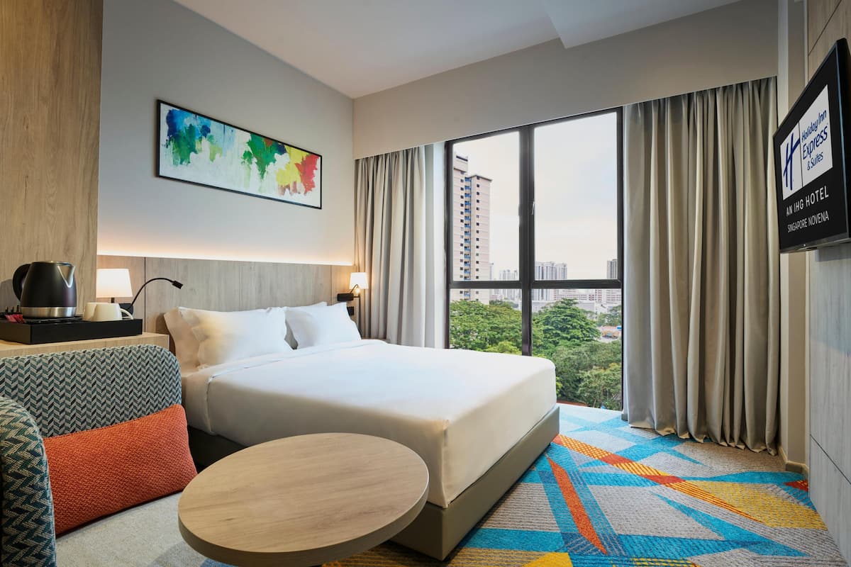 Une chambre d’hôtel avec un lit, un canapé, une table ronde, un tableau et une vue sur la ville.