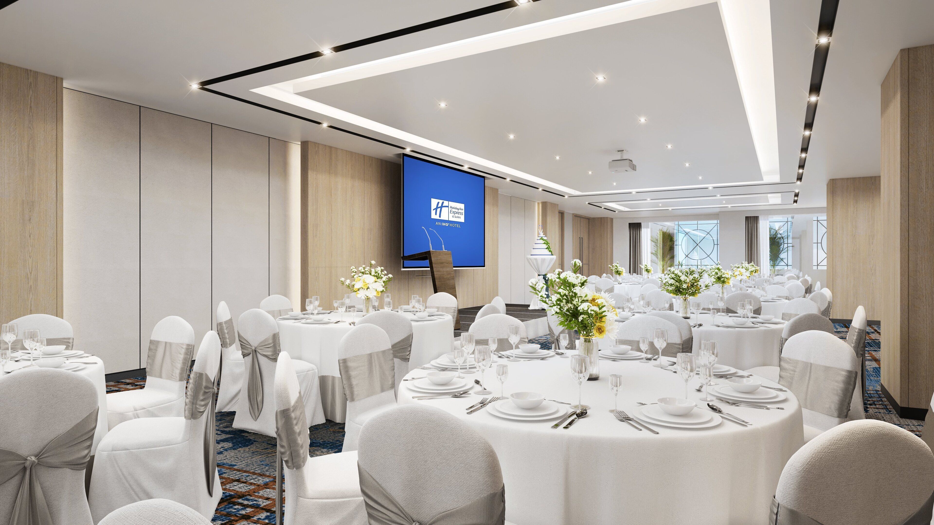 A conference room with multiple round tables set for dining, white chairs, and a large screen displaying a presentation.