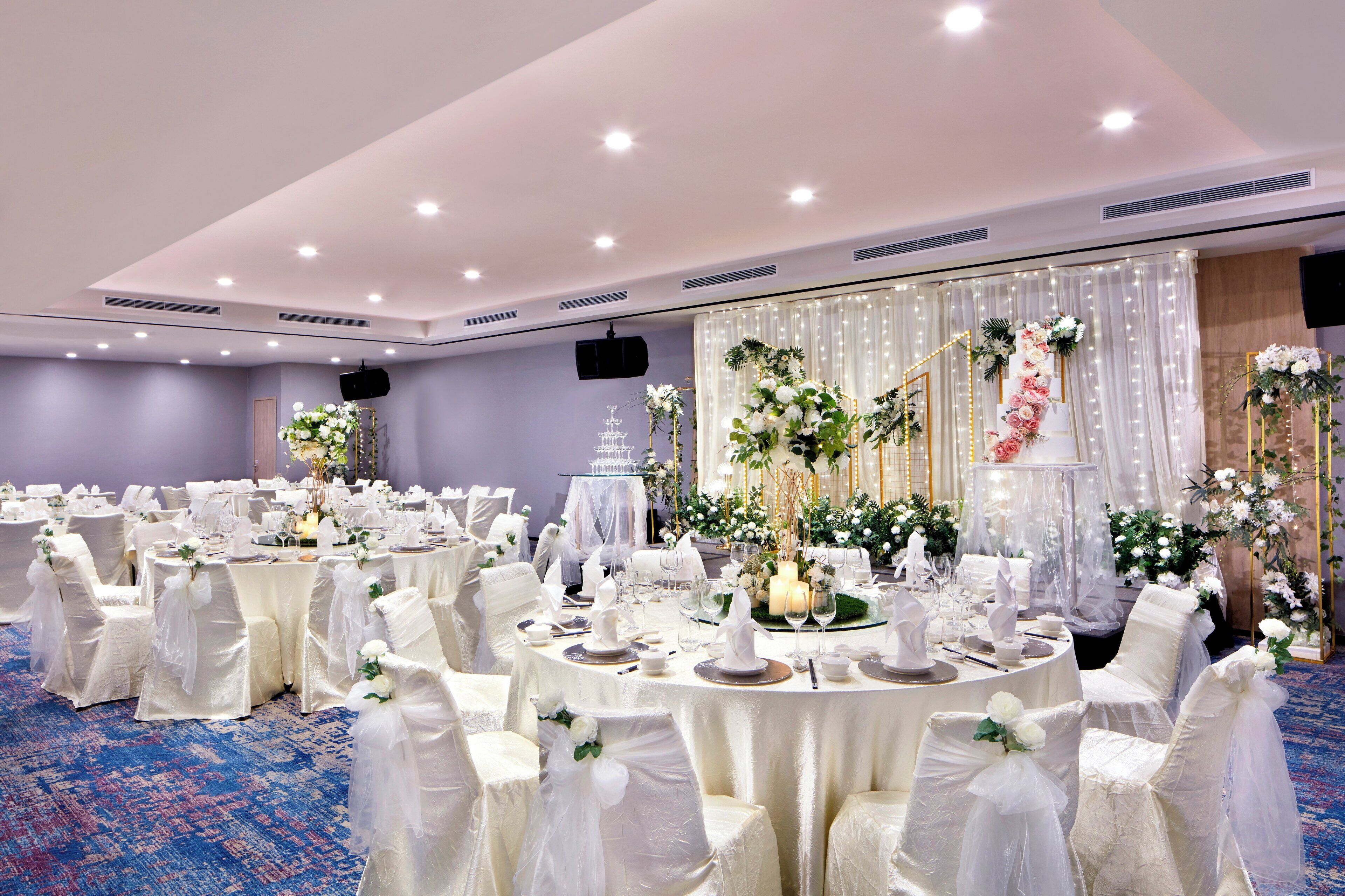 Une salle de banquet avec des tables rondes dressées pour un événement formel, décorées de nappes blanches et agrémentées de compositions florales.