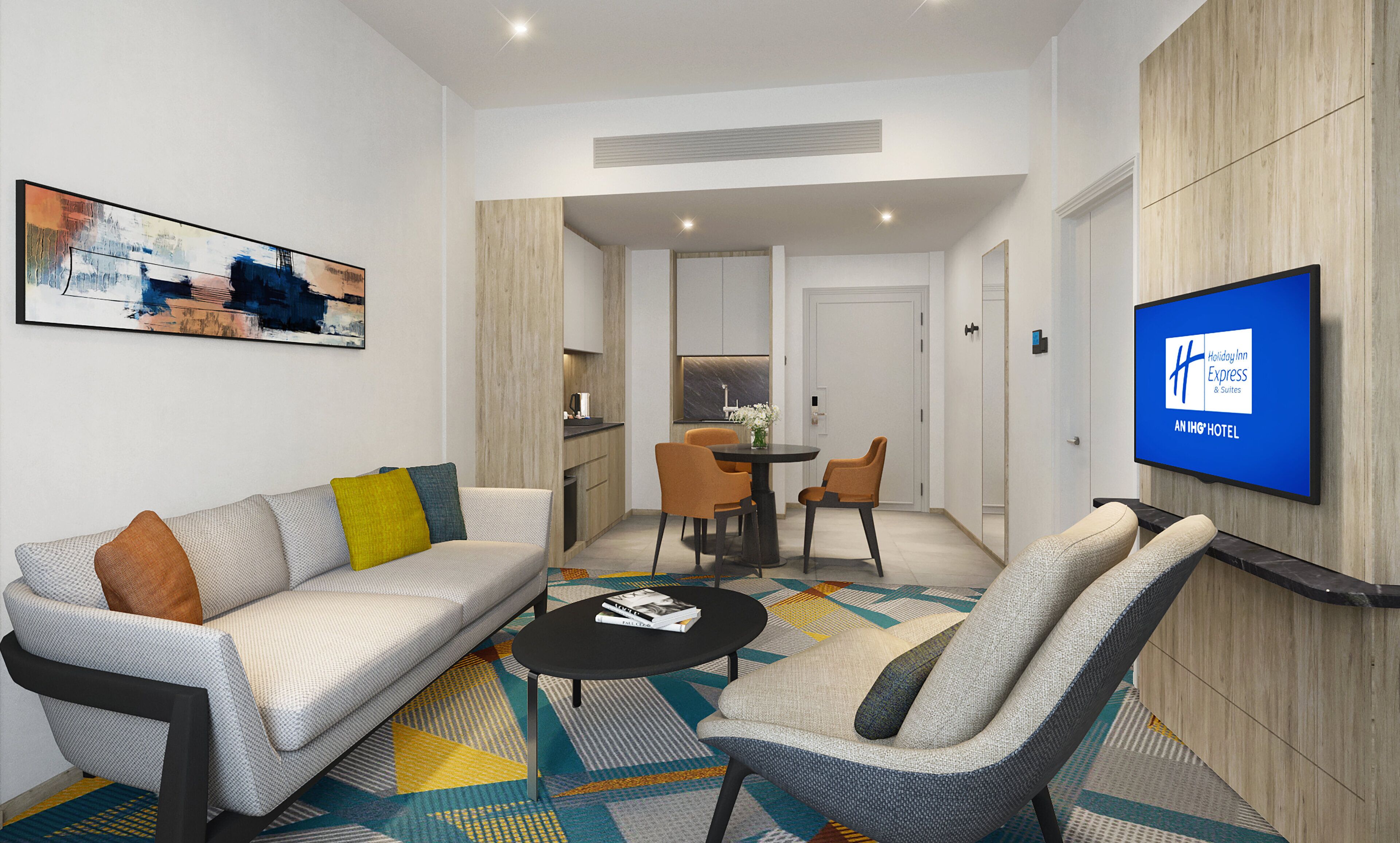 Et moderne hotelværelse med sofa, lænestol, spisebord og et tv, der viser hotellets navn.