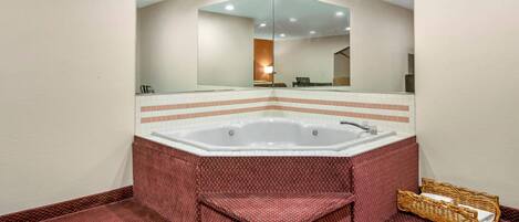 A bathroom with a large bathtub, a mirror, and a wicker basket.