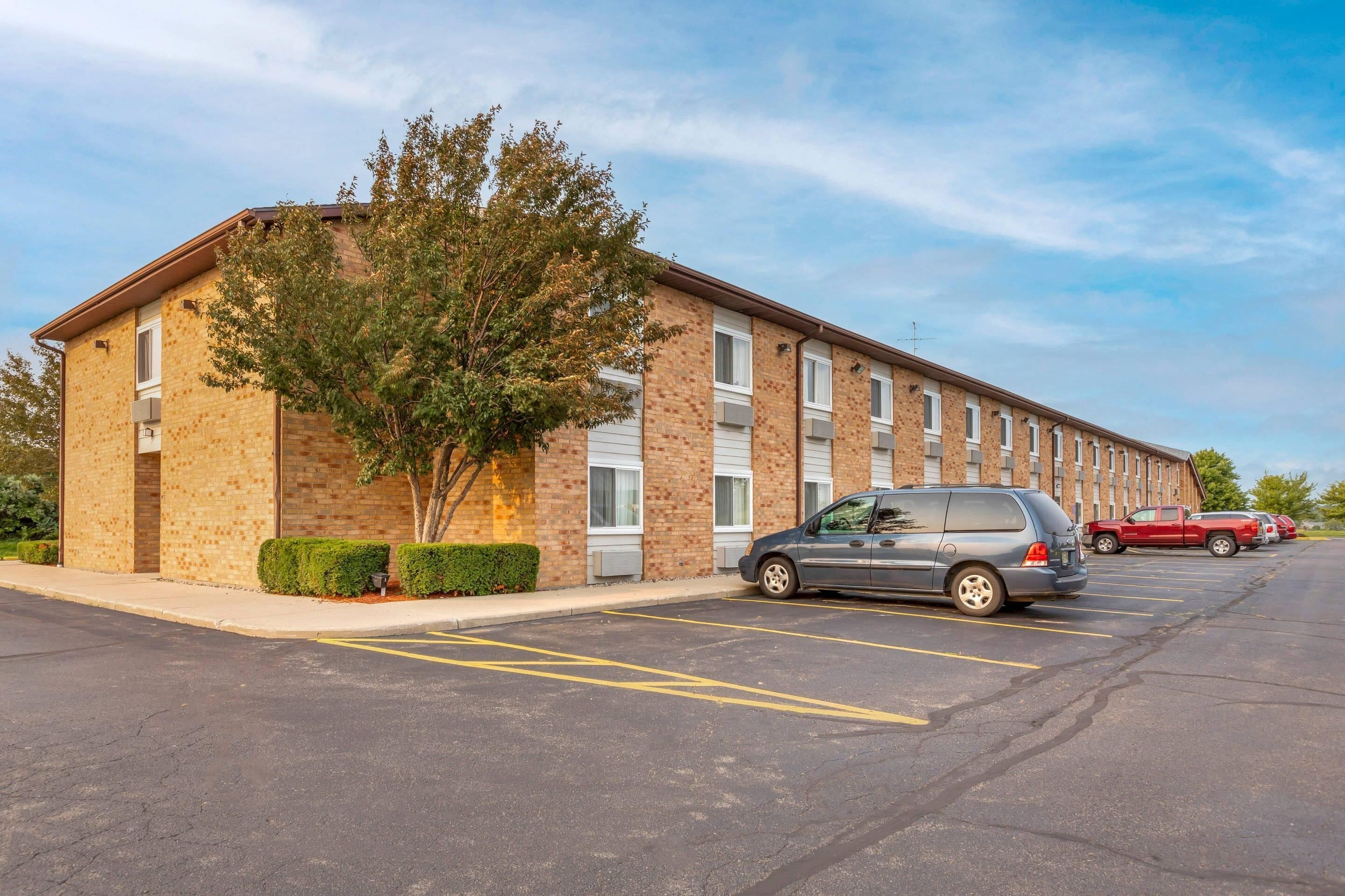 A multi-story brick building with a parking lot, a tree, and a parked car.