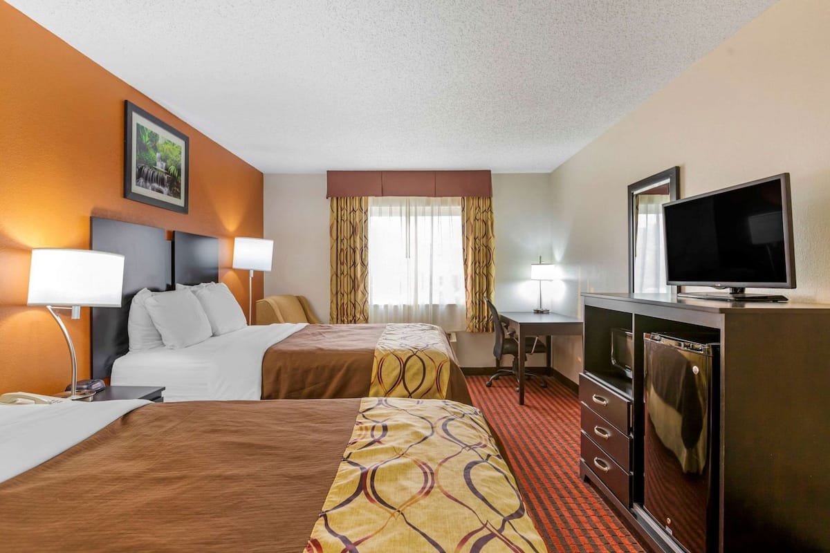 A hotel room with two beds, a desk, a TV, and a minibar.