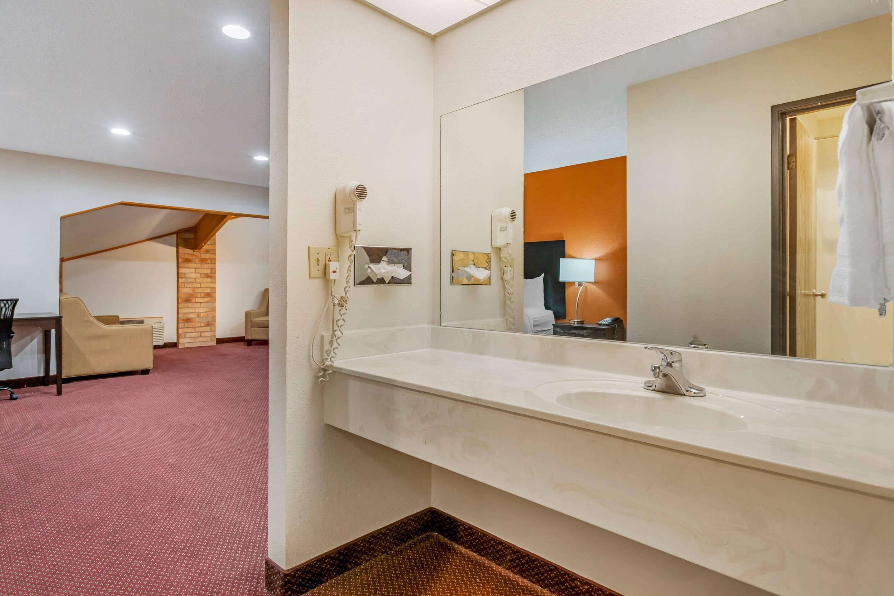 A hotel bathroom with a large mirror, a sink, and a hairdryer.