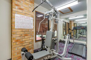 A fitness center with exercise equipment, a treadmill, and a brick wall. - Rodeway Inn Coopersville (Coopersville)